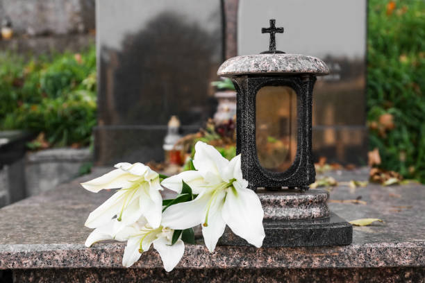 White lilies and grave light on granite tombstone outdoors. Funeral ceremony White lilies and grave light on granite tombstone outdoors. Funeral ceremony
